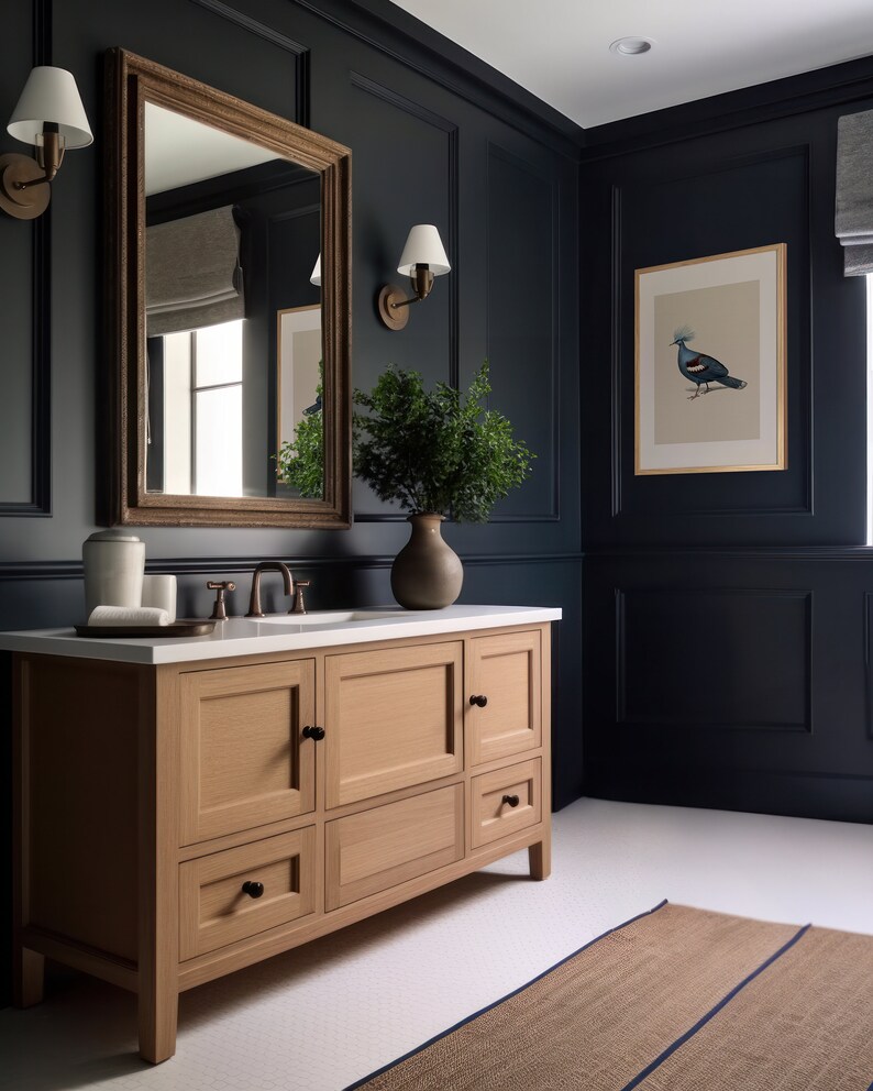 Puede incluir: Un tocador de ba&ntilde;o de madera clara con tres cajones y dos gabinetes. El tocador tiene herrajes negros y una encimera blanca. El tocador est&aacute; en un ba&ntilde;o azul oscuro con una impresi&oacute;n enmarcada de un p&aacute;jaro y un espejo sobre el tocador.