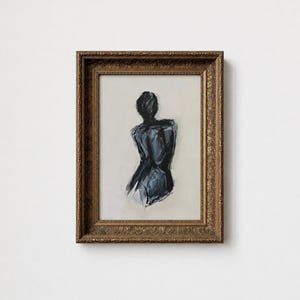 May include: An abstract painting of a figure in a dark blue hue, viewed from the back. The artwork is framed in a gold-colored, ornate frame. The background is a light beige color.