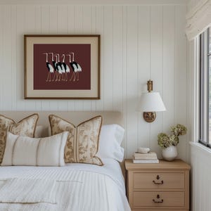 May include: A white bed with a white and brown patterned throw blanket and a white and brown patterned pillow. There is a framed print of black and white birds on a maroon background above the bed. A nightstand with three drawers is on the right side of the bed.