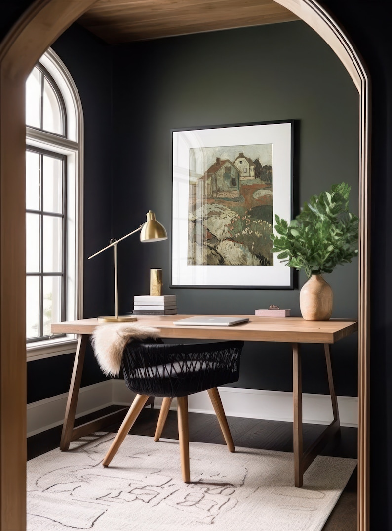 Puede incluir: Una oficina en casa con una pared verde oscuro, un escritorio de madera con una silla negra tejida, una l&aacute;mpara dorada y una pintura de paisaje enmarcada. Un jarr&oacute;n con hojas verdes se encuentra en el escritorio.