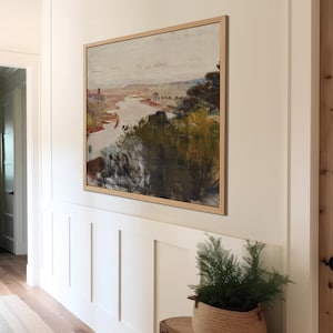 Puede incluir: Una pintura de paisaje enmarcada con un r&iacute;o serpenteando a trav&eacute;s de un paisaje verde y marr&oacute;n. La pintura est&aacute; colgada en una pared blanca con z&oacute;calos blancos.