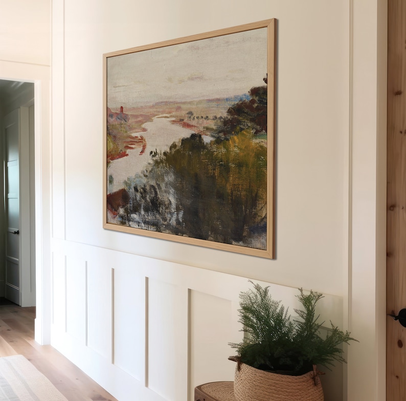 Puede incluir: Una pintura de paisaje enmarcada con un r&iacute;o serpenteando a trav&eacute;s de un paisaje verde y marr&oacute;n. La pintura est&aacute; colgada en una pared blanca con z&oacute;calos blancos.
