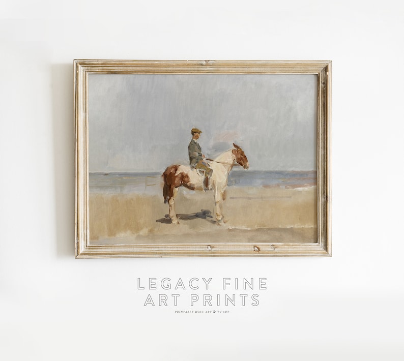 May include: A framed painting of a person riding a brown and white horse on a beach. The sky is a light blue and the water is a light gray. The painting is in a light wood frame.