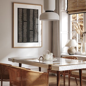 May include: A dining room with a white table with a white and gold inlay design. The table has a glass top and is surrounded by four wicker chairs. A white pendant light hangs above the table. A black and white abstract print hangs on the wall behind the table.