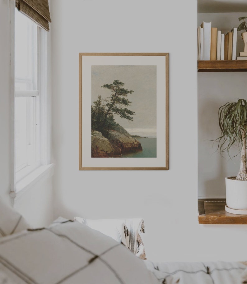 May include: A framed print of a painting depicting a lone pine tree growing on a rocky cliff overlooking a body of water. The sky is a muted gray, and the water is a deep blue.