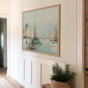 K&ouml;nnte beinhalten: Ein gerahmtes Gem&auml;lde, das eine Meereslandschaft mit mehreren Segelbooten zeigt, die an einem Pier festgemacht sind. Das Gem&auml;lde ist in einem hellen Holzrahmen gefasst und h&auml;ngt an einer wei&szlig;en Wand.