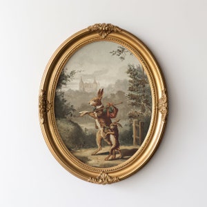 May include: A vintage oval-shaped framed painting of two rabbits walking through a forest. The rabbits are brown and white, and the larger rabbit is wearing a brown jacket and carrying a bag. The painting is set against a backdrop of a forest with a castle in the distance.