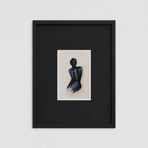 May include: A framed abstract art print. The artwork depicts a dark blue figure with a neutral background. The print is set within a white mat and a black frame, creating a striking contrast. The artwork is a minimalist representation of the human form.