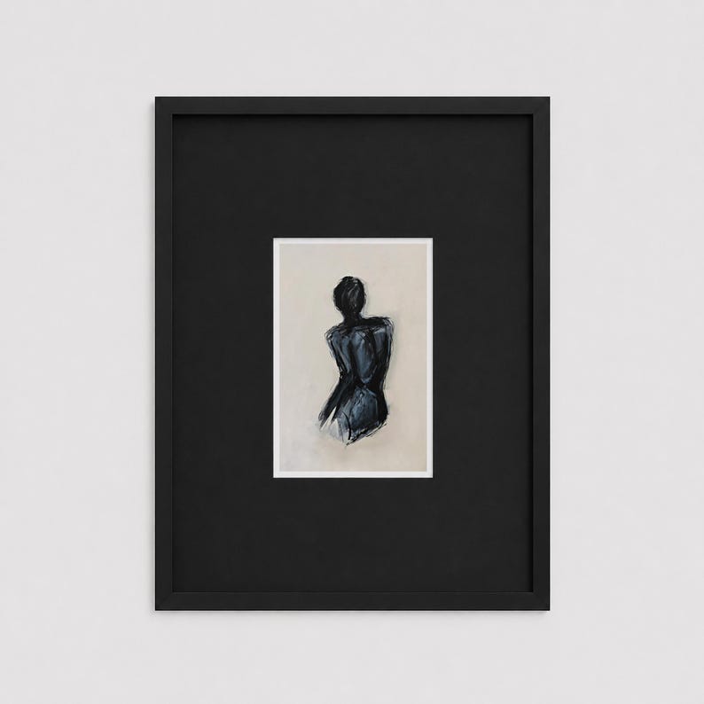 May include: A framed abstract art print. The artwork depicts a dark blue figure with a neutral background. The print is set within a white mat and a black frame, creating a striking contrast. The artwork is a minimalist representation of the human form.