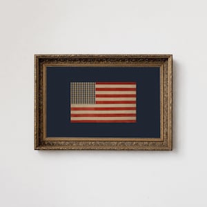 Puede incluir: Obra de arte enmarcada con un diseño vintage de la bandera estadounidense. La bandera tiene un fondo azul marino con un patrón de cuadros en la esquina superior izquierda y rayas rojas y blancas. El marco es ornamentado con un acabado dorado.