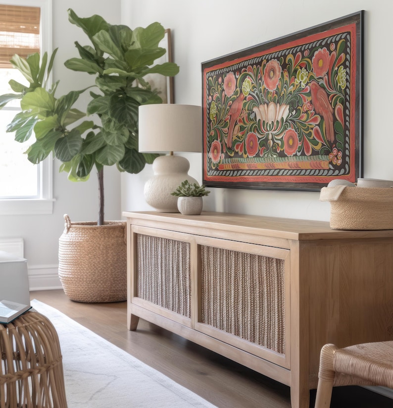 Puede incluir: Una consola de madera clara con dos puertas de rat&aacute;n. La consola est&aacute; decorada con una gran pintura enmarcada de flores y p&aacute;jaros coloridos. Una gran planta de ficus lyrata en maceta se encuentra a la izquierda de la consola.