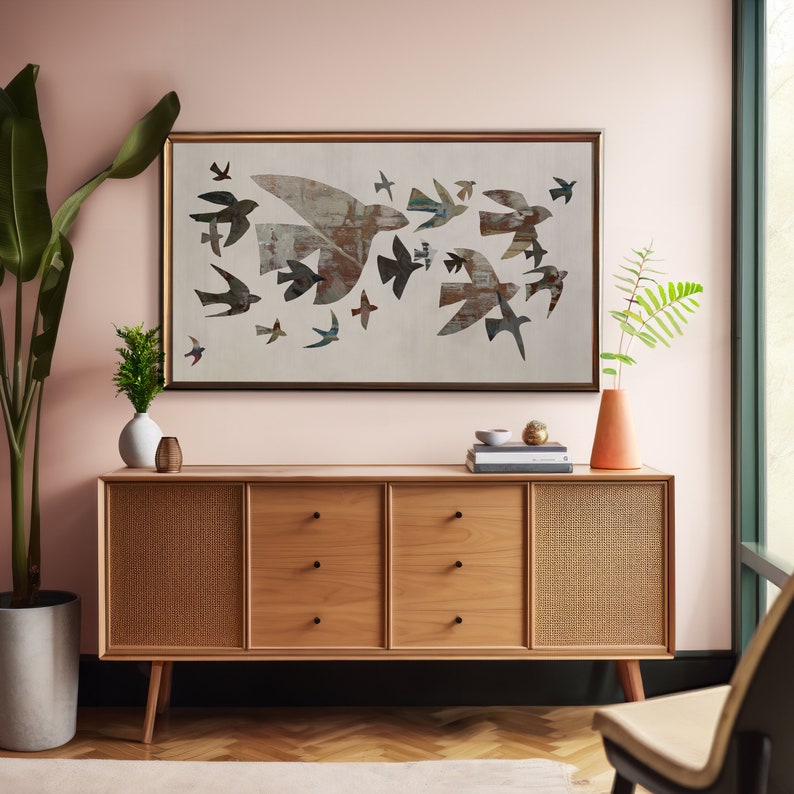 May include: A mid-century modern style wooden sideboard with three drawers and two woven cane door panels. Above the sideboard is a framed artwork featuring a flock of stylized birds in flight, in shades of brown, gray, and blue. A tall potted plant and vase are on either side.
