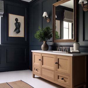 May include: A bathroom with navy blue walls, a light wood vanity with a white countertop, and a large framed mirror. A framed sketch hangs on the wall. A woven rug with blue trim is on the floor.
