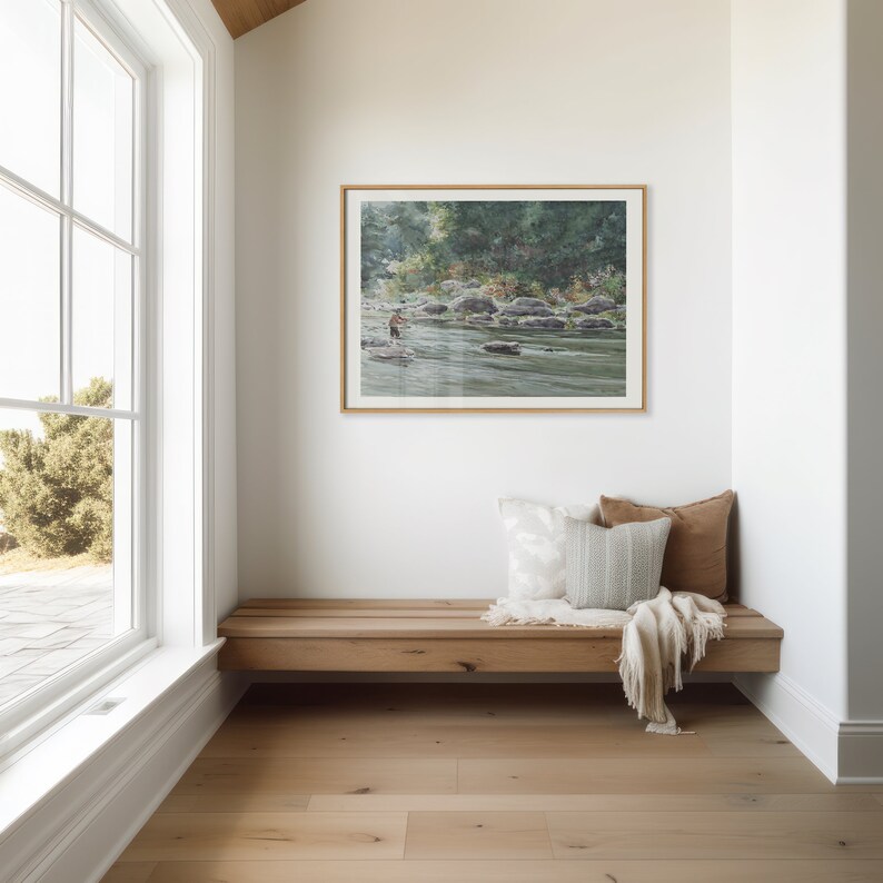 May include: A wooden bench with two pillows and a throw blanket sits in a corner of a room with a large window and a framed watercolor painting of a river scene.