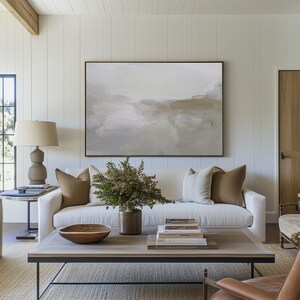Peut inclure: Un canap&eacute; blanc avec des coussins marrons se trouve dans un salon avec une grande peinture abstraite au mur au-dessus. Une table basse avec des livres et un bol en bois se trouve devant le canap&eacute;.
