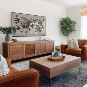 May include: A living room scene featuring a large wooden cabinet, a coffee table, and two leather armchairs. A framed artwork of birds in flight hangs above the cabinet. Decorative vases and a plant add to the room's aesthetic.