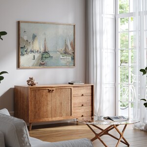 K&ouml;nnte beinhalten: Ein Wohnzimmer im Stil der Mid-Century Modern mit einem Schrank aus Holz mit einer T&uuml;r aus geflochtenem Rattan, einem Glas-Couchtisch und einem gerahmten Gem&auml;lde von Segelbooten in einem Hafen.