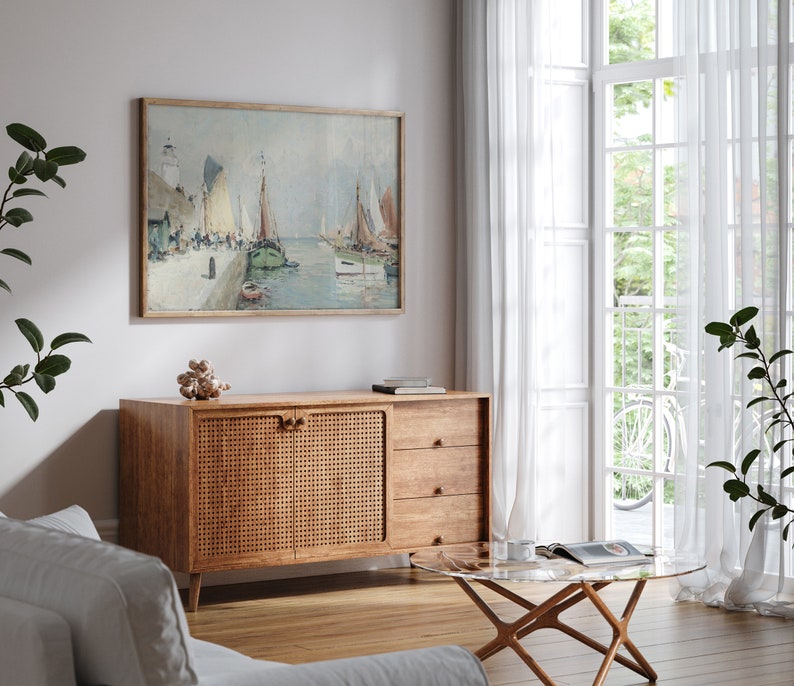 K&ouml;nnte beinhalten: Ein Wohnzimmer im Stil der Mid-Century Modern mit einem Schrank aus Holz mit einer T&uuml;r aus geflochtenem Rattan, einem Glas-Couchtisch und einem gerahmten Gem&auml;lde von Segelbooten in einem Hafen.