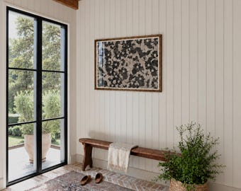 May include: A rectangular framed wall art piece featuring a black and white floral pattern hangs above a long wooden bench. A light-colored textile is draped over the bench, with a pair of brown slip-on shoes placed on the floor nearby.
