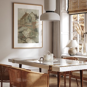 Puede incluir: Una l&aacute;mpara colgante de cer&aacute;mica blanca cuelga sobre una mesa de comedor con una tapa de m&aacute;rmol blanco y una silla de rat&aacute;n tejido. La mesa est&aacute; puesta con una tetera blanca y un plato blanco. Una impresi&oacute;n enmarcada de una pintura de paisaje cuelga en la pared detr&aacute;s de la mesa.