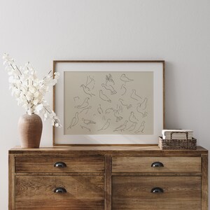 May include: A framed print of a minimalist line drawing of multiple birds in various poses, hanging on a wall above a wooden dresser with two drawers.