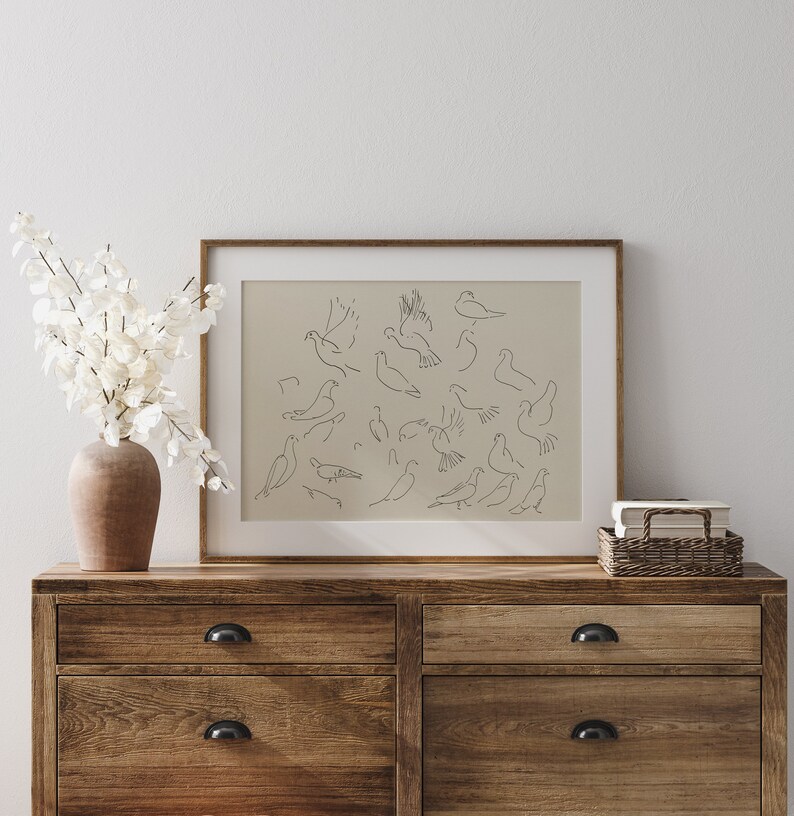 May include: A framed print of a minimalist line drawing of multiple birds in various poses, hanging on a wall above a wooden dresser with two drawers.