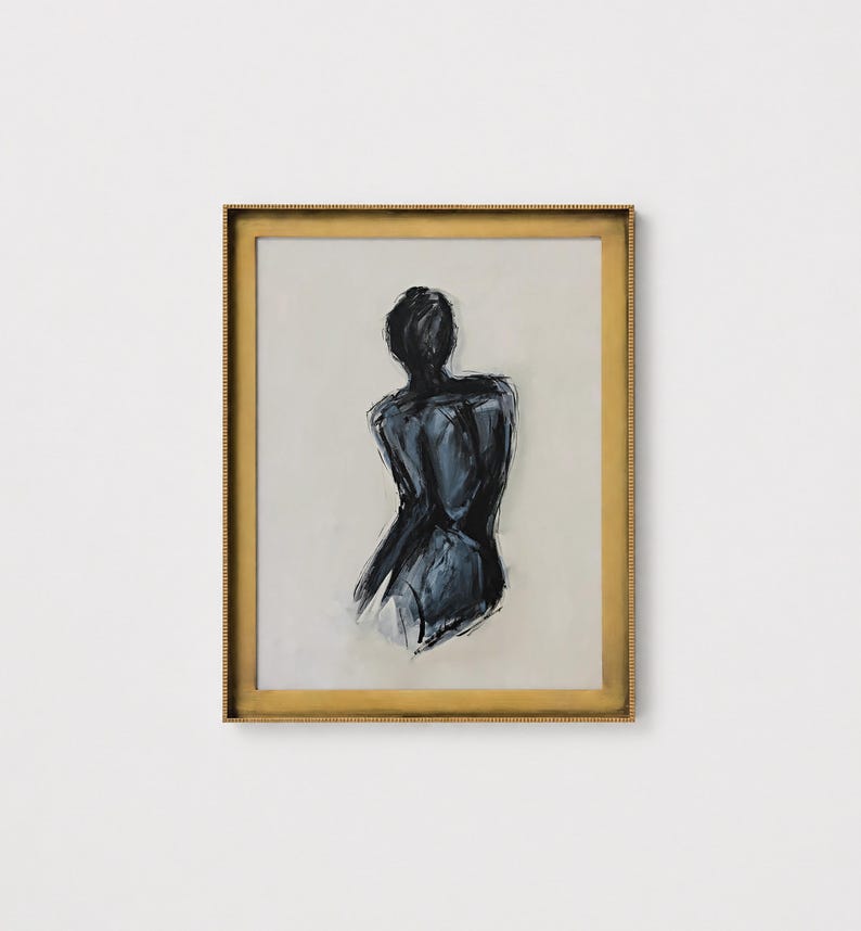 May include: Abstract art print featuring a figure's back in shades of black and gray. The artwork is framed in a gold-colored, ornate frame. The background is a neutral beige color, creating a contrast with the dark figure.