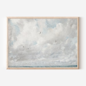 May include: A framed print featuring a vintage-style landscape painting. The artwork depicts a cloudy sky with shades of gray and blue, and several birds in flight. The print is encased in a light brown wooden frame.