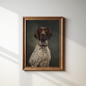 Op de afbeelding: Een ingelijst portret van een Duitse Staande Hond. De hond heeft bruin en wit gevlekte vacht, bruine oren en een bruine halsband. Het kunstwerk staat tegen een donkergroene achtergrond en is ingelijst in een houten lijst.
