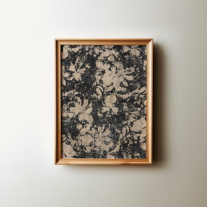 May include: A framed print featuring a black and white floral design. The flowers are stylised and have a distressed appearance. The frame is a light wood colour.