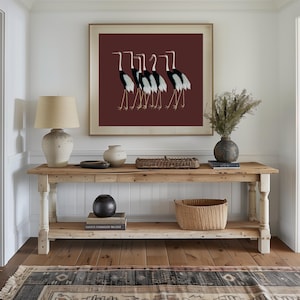 May include: A wooden console table with two shelves, a wicker basket, a black ceramic vase, and a framed print of a group of black and white cranes on a burgundy background.