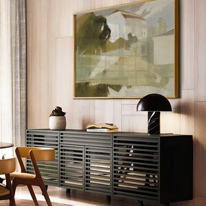 May include: A black cabinet with slatted doors and a wood top. The cabinet is in a modern living room with a large abstract painting on the wall behind it. A lamp with a black shade sits on the cabinet.