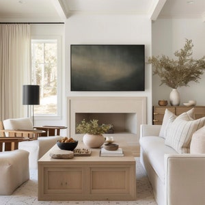 May include: A living room with a white couch, a coffee table, and a fireplace. The fireplace has a painting above it and a plant in front of it. There is a lamp and a chair in the corner of the room.