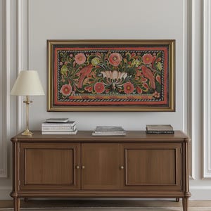 Puede incluir: Un armario de madera con tres puertas y pomos de lat&oacute;n. El armario es marr&oacute;n y tiene un borde decorativo alrededor de los bordes. Hay libros en la parte superior del armario y una pintura enmarcada de un dise&ntilde;o floral con p&aacute;jaros en la pared sobre el armario.