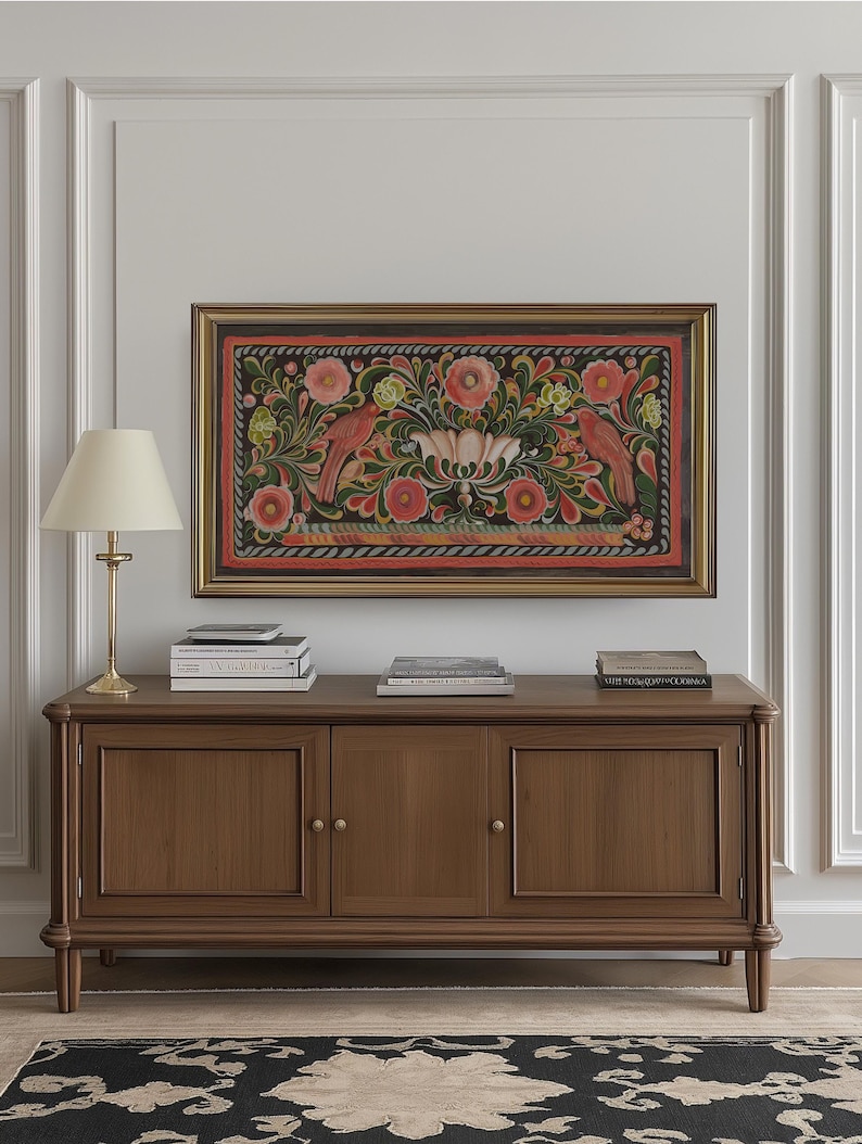 Puede incluir: Un armario de madera con tres puertas y pomos de lat&oacute;n. El armario es marr&oacute;n y tiene un borde decorativo alrededor de los bordes. Hay libros en la parte superior del armario y una pintura enmarcada de un dise&ntilde;o floral con p&aacute;jaros en la pared sobre el armario.