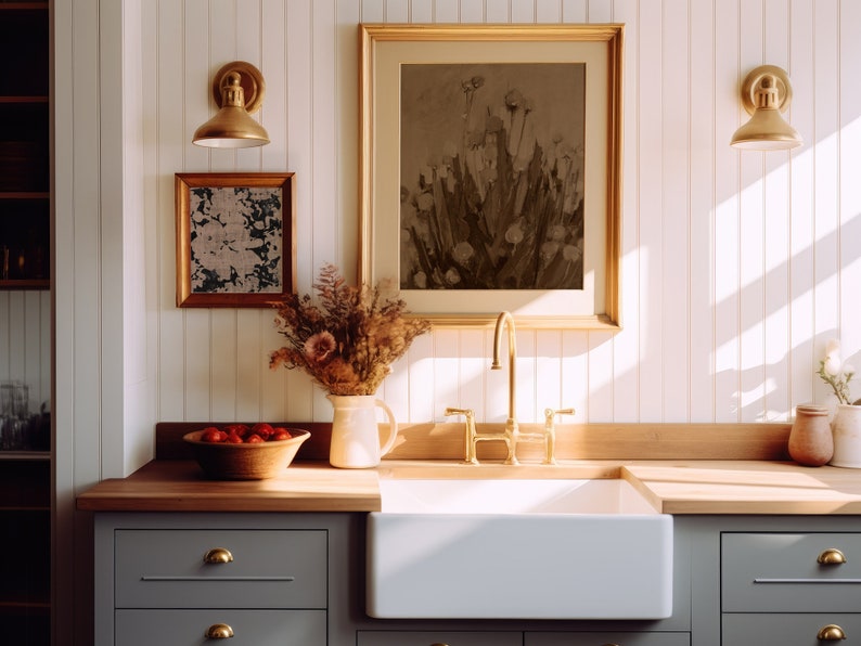 May include: A white farmhouse kitchen sink with a gold tap and a wooden worktop. A framed print of a floral still life hangs above the sink.