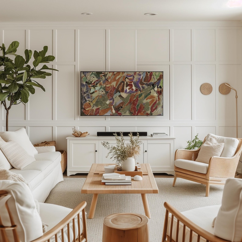 May include: A light and airy living room with white walls and furniture. An abstract painting hangs above a white cabinet. A light wood coffee table sits in front of a white sofa and rattan chairs. A large green plant is in the corner.