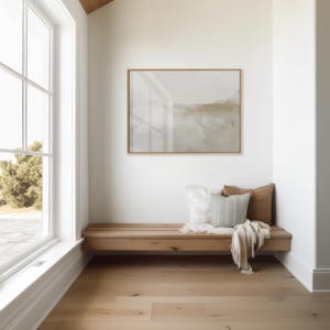 Peut inclure: Un banc en bois avec une finition brun clair se trouve dans un coin d'une pi&egrave;ce aux murs blancs. Le banc est dot&eacute; de trois coussins, un blanc, un gris clair et un brun. Une couverture blanche est jet&eacute;e sur le banc. Un tableau abstrait encadr&eacute; est accroch&eacute; au mur au-dessus du banc.