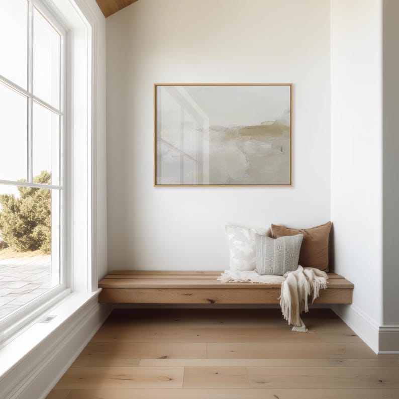 Peut inclure: Un banc en bois avec une finition brun clair se trouve dans un coin d'une pi&egrave;ce aux murs blancs. Le banc est dot&eacute; de trois coussins, un blanc, un gris clair et un brun. Une couverture blanche est jet&eacute;e sur le banc. Un tableau abstrait encadr&eacute; est accroch&eacute; au mur au-dessus du banc.