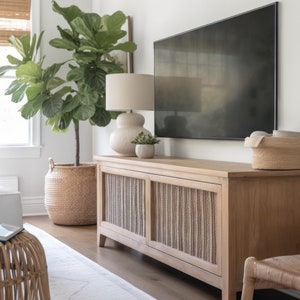 May include: A light wood media console with two doors featuring a woven rattan design. The console is topped with a cream-colored lamp, a small potted plant, and a flat-screen TV.