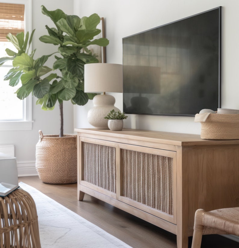 May include: A light wood media console with two doors featuring a woven rattan design. The console is topped with a cream-colored lamp, a small potted plant, and a flat-screen TV.