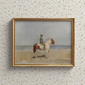 May include: A framed painting of a person riding a brown and white horse on a beach. The painting is in a gold frame and has a light blue sky in the background.