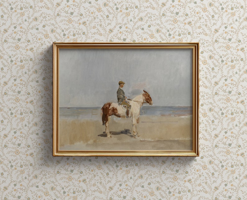 May include: A framed painting of a person riding a brown and white horse on a beach. The painting is in a gold frame and has a light blue sky in the background.