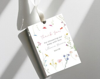 May include: A white tag with a floral border and the words "Thank You" in pink script. The tag includes the text "For showering our baby with love" and the name "Lilliana Stevens" with the date "JULY 20".