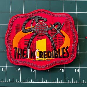 May include: A red, white, and black embroidered patch with a chain border. The patch features a cartoon image of a robot with a globe on its head and the text "THE INCREDIBLES EST. APRIL 2 1948".