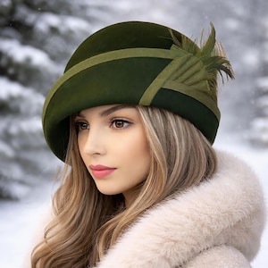 May include: A dark green cloche hat with a decorative feather accent. The hat features a contrasting band and trim in a lighter shade of green. The hat is a vintage style, perfect for a winter look.