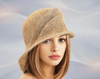 May include: A woven straw hat with a unique asymmetrical design. The hat is a light tan color and has a brim that curves upwards on one side. The hat is a stylish accessory.