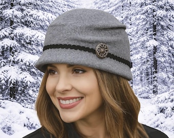 May include: A gray cloche hat with a black trim and a decorative button. The hat is made of a soft material and has a rounded crown and a small brim. The hat is a stylish accessory for cold weather.