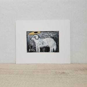 May include: An original painting of a white dog with a gold halo, set against a black and gray background. The artwork is matted in a white frame, creating a striking contrast. The dog's fur is textured, and the halo adds a touch of whimsy.