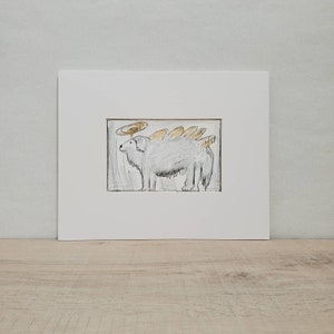 May include: A black and white drawing of a dog with a halo above its head and a series of golden wings on its back. The drawing is framed in a white mat.
